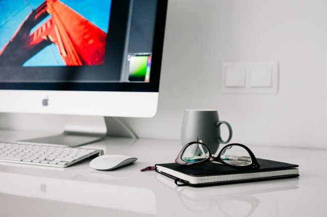 Desk with Mac. glasses and book.
